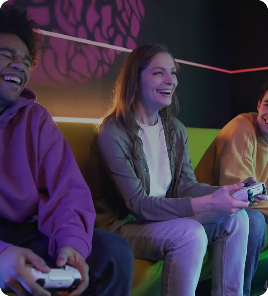 Drie vrienden zitten samen op een bank en spelen een game met controllers, terwijl ze lachen en ontspannen in een gamingomgeving.